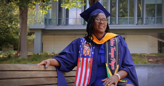 Patrice wearing Commencement gown and cap smiling on campus